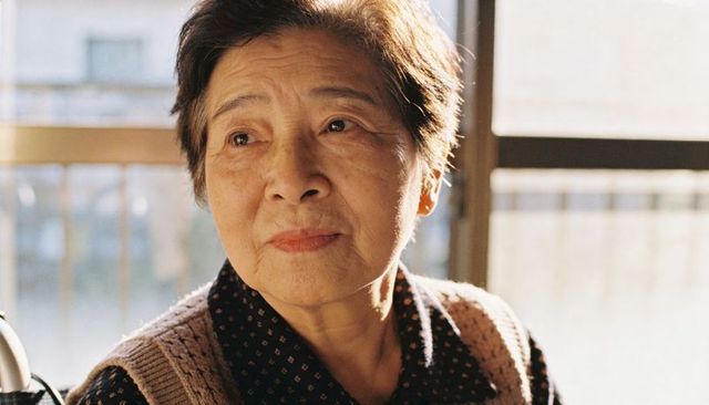Elderly asian woman gazing out window backlit portrait conveying quiet contemplation
