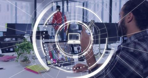 Creative professional holding smartphone working at open-plan desk with HUD overlay