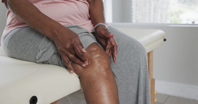 Senior woman massaging her knee at home to soothe joint pain. Useful for healthcare promotions, articles related to elderly care, physical therapy advertising, and educational materials about arthritis and self-care.