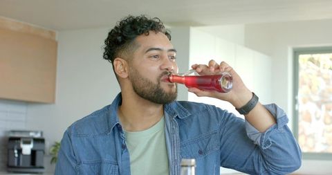 Man drinking red beverage at modern kitchen counter wearing denim shirt