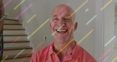 Smiling senior man standing in welcoming foyer wearing coral polo with pastel stripe overlay