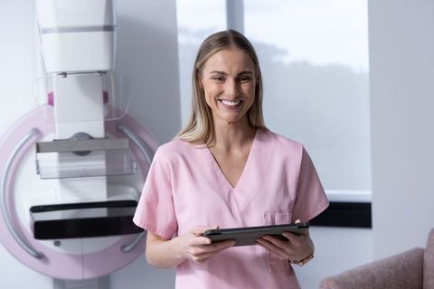Smiling radiology technician standing by mammography unit holding tablet