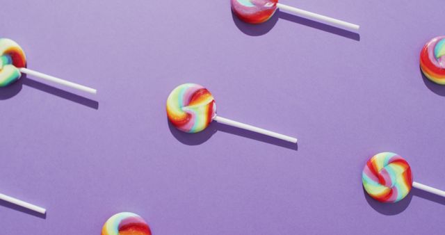 A visually striking arrangement of vibrant, multicolored lollipops on a violet background, placed in a geometric pattern. This fun and cheerful image is ideal for use in advertising confectionery products, event planning for children's parties, or creating eye-catching social media content. Perfect for designs related to celebrations, fun, and indulgence.