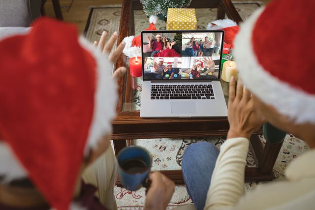 Diverse couple wearing Santa hats having a video call with friends on laptop, celebrating Christmas together virtually. Perfect for illustrating remote holiday celebrations, virtual New Year parties, festive digital greetings, and online holiday communication.