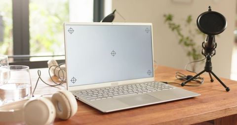 Slim silver laptop with headphones and microphone on wooden home office desk for podcasting