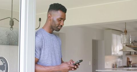 Man standing at sliding glass door checking smartphone in modern minimalist kitchen
