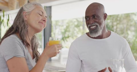 Mature couple enjoying morning orange juice at sunlit kitchen bar, relaxed lifestyle