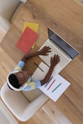 African american boy studying online with headphones and laptop on wooden table