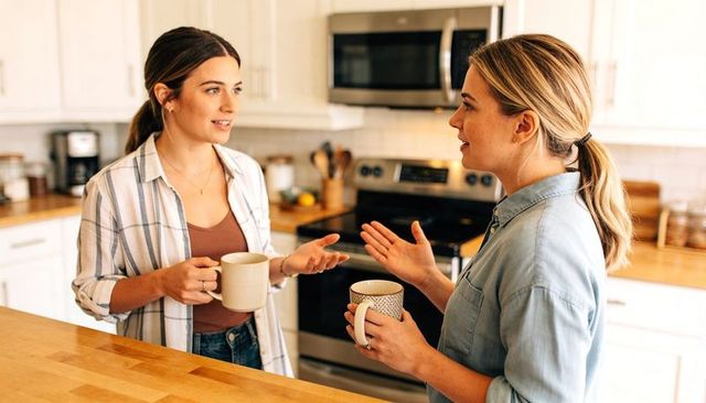 Two women chatting over coffee at kitchen island, casual friends sharing conversation and smiles