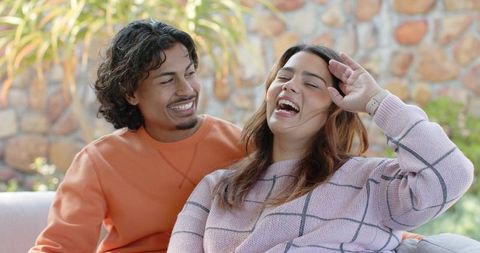Laughing young couple relaxing on outdoor patio couch during sunny daylight moment