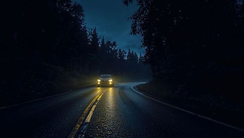 Headlights cutting through mist on wet curvy forest road at night, double yellow lines