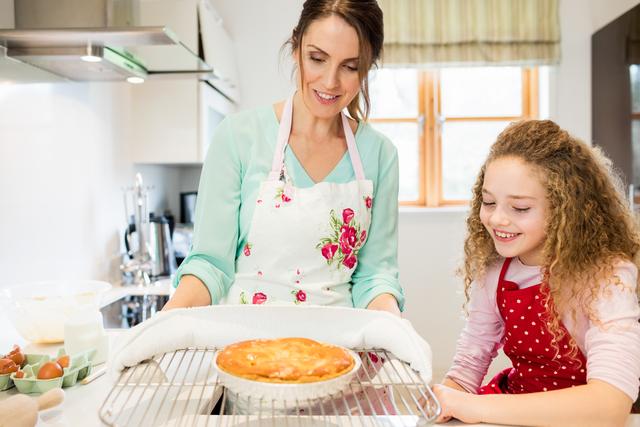 Mother interacting with daughter while holding pancake in cooling rack at kitchen