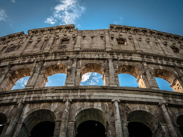 This image showcases the imposing structure of the Roman Colosseum from a low angle, highlighting its architectural grandeur against a clear blue sky. It is ideal for use in travel publications, educational materials on Roman history, or historical architecture presentations.