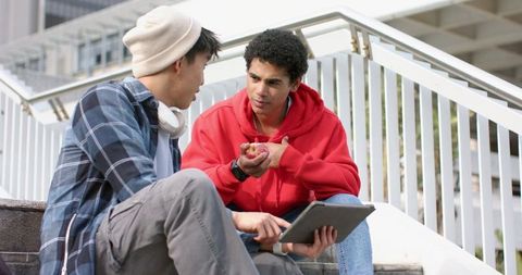 Asian and african american students studying on campus steps sharing tablet and apple