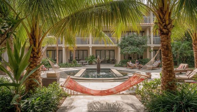 Orange hammock swaying between palm trees framing resort courtyard fountain and loungers