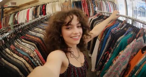 Curly-haired woman exploring boutique rack with smartphone