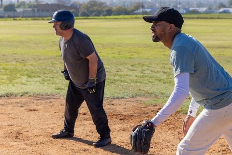 Senior player and teammate practicing base running and fielding on sunny community diamond