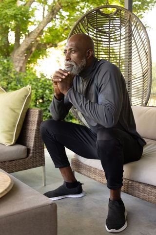 Senior african american man sitting on porch sofa, leaning, gazing thoughtfully in garden