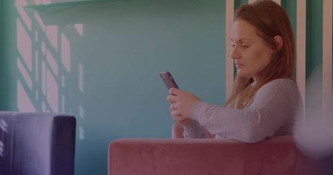 Casual woman scrolling smartphone on pink chair with teal wall shadows and copy space