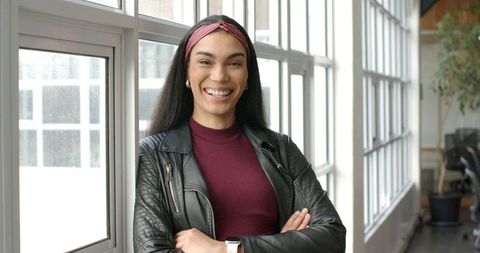 Confident presenter leaning on window with arms crossed, smiling in modern office studio