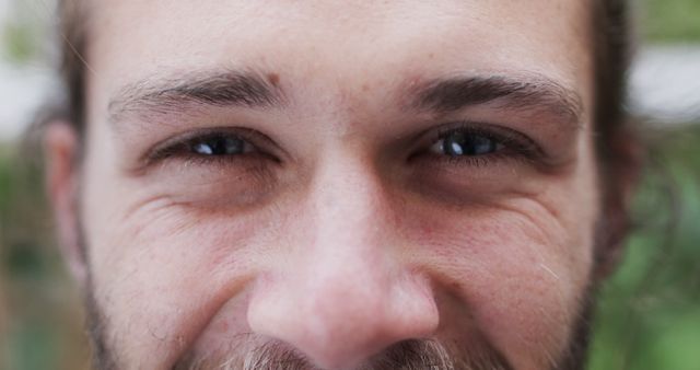 Showing details of a young man's face with a focus on his eyes and smile. Can be used for advertising healthy lifestyle, positive emotions, or personal care products considering the detail in the skin and expression.