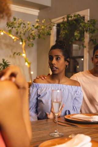 Supportive shoulder touch during intimate dinner conversation with warm mood lighting
