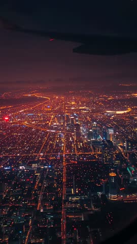 Vertical video flying over illuminated city grid at dusk showing wing and winding highway