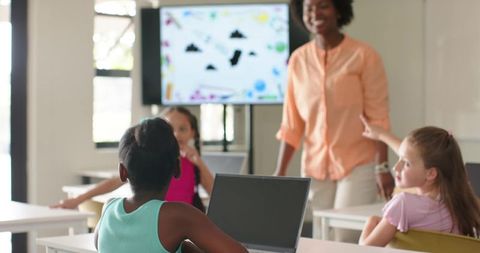 Diverse female teacher engaging teenage students with laptops in modern classroom