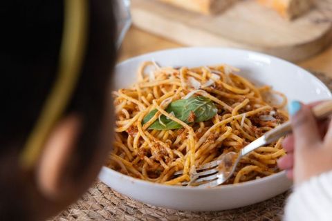 Child twirling spaghetti with basil, turquoise nails, warm cozy home dinner closeup
