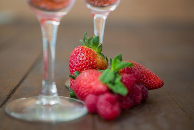 Fresh strawberries and raspberries placed on a wooden table with two cocktail glasses in the background. Ideal for use in food and drink blogs, healthy eating promotions, summer recipes, and organic produce advertisements.