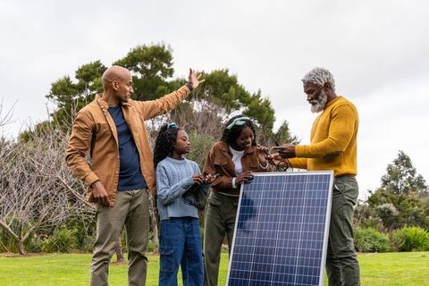 Multigenerational african american family installing freestanding solar panel in backyard