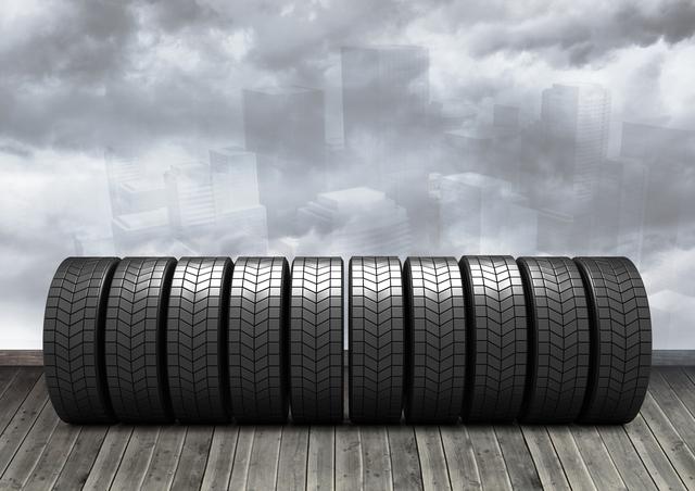 Image of tires neatly arranged in a row on a wooden plank floor with a cloudy urban backdrop, ideal for use in automotive advertisements, transportation industry promotions, retail tire shop displays, and web graphics highlighting vehicle maintenance products.
