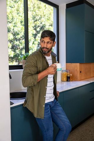 Man in modern kitchen holding mug checking smartphone near window
