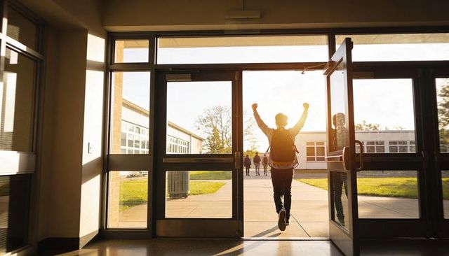 Teen celebrating end of school day running through glass doors into sunlit campus courtyard