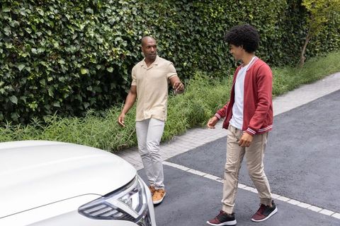 African american friends walking to white suv on driveway near ivy hedge wearing sneakers