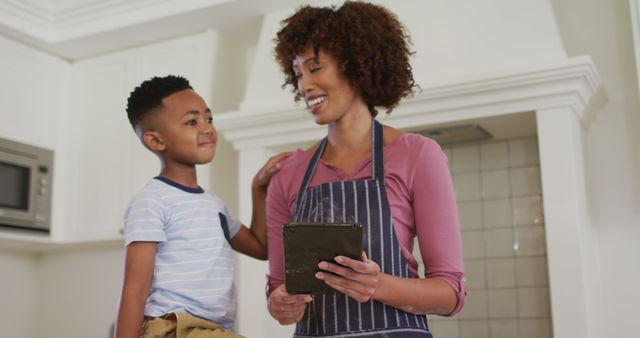 African american mother and son in kitchen cooking, looking at tablet - Download Free Stock Photos Pikwizard.com