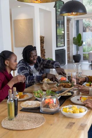 African american friends sharing roasted bird at wooden dining table for cozy family feast