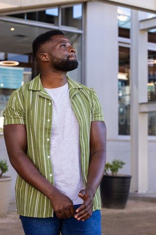 African man standing at modern commercial building wearing green striped shirt gazing up