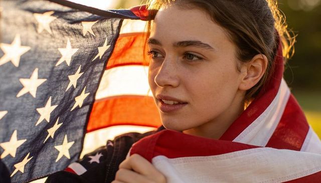 Young woman wrapping herself in american flag at golden hour expressing patriotism