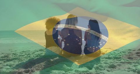 Three women sitting on sandy beach watching sunset with brazilian flag overlay, friendship