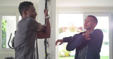 Personal trainer coaching client stretching shoulders in modern home gym with smartwatch