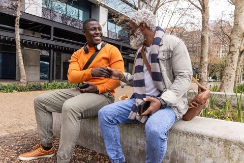 African american young man and older man laughing and fist-bumping on urban campus bench