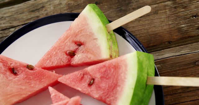 Slices of watermelon are creatively served on popsicle sticks, making them look like watermelon popsicles, with copy space. This presentation offers a fun and refreshing way to enjoy a summer fruit favorite.
