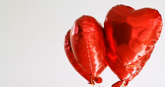 Two red heart-shaped balloons are floating against a light background, with copy space. They symbolize love and celebration, often used for romantic occasions such as Valentine's Day or anniversaries.