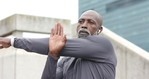 Senior african american man stretching shoulder outdoors wearing smartwatch and earbuds