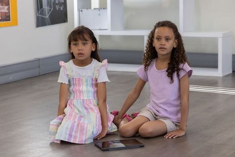 Diverse girls sitting on classroom floor with tablet focused on learning and friendship