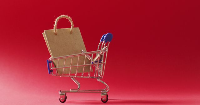 Miniature shopping cart with a paper bag inside on a red background conveys themes of retail, shopping, and consumerism. It can be used in marketing materials for sales, promotions, consumer behavior studies, or retail advertisements.