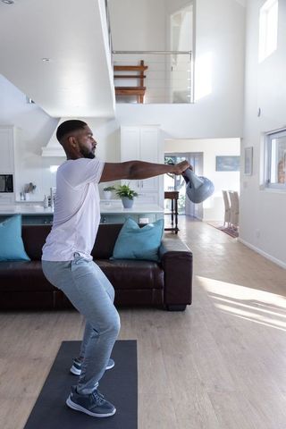 Man Performing Kettlebell Swing in Bright Living Room