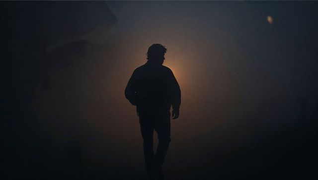 Backlit male silhouette walking through misty night with halo light, cinematic moody scene