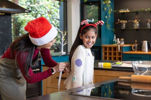 Indian mother and daughter baking cookies together wearing santa hat and candy-cane headband